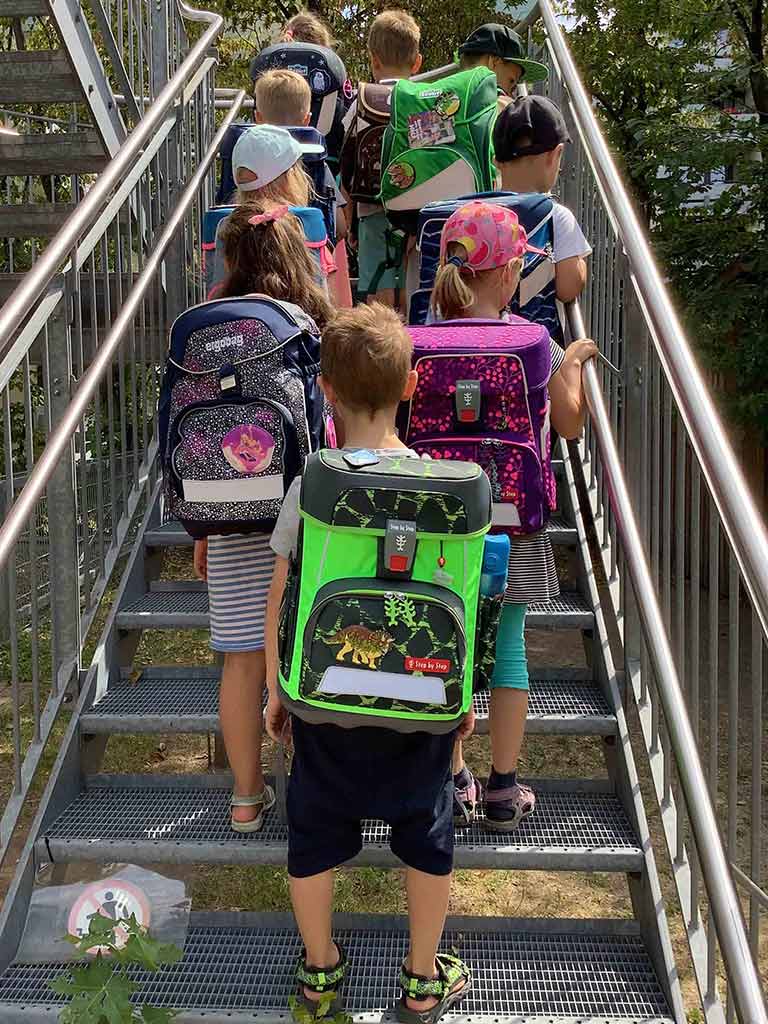 Kindergartenkinder stehen an einer Treppe und zeigen ihre zukünftigen Schulranzen